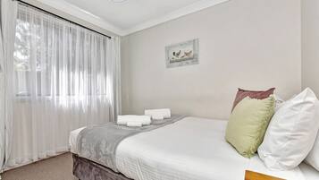A bedroom with a bed, a window with sheer curtains, a wall-mounted picture, and a carpeted floor.