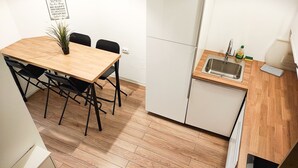 Kompakti keittiö, jossa on puinen ruokapöytä, mustat tuolit, pieni pesuallas ja valkoinen jääkaappi.