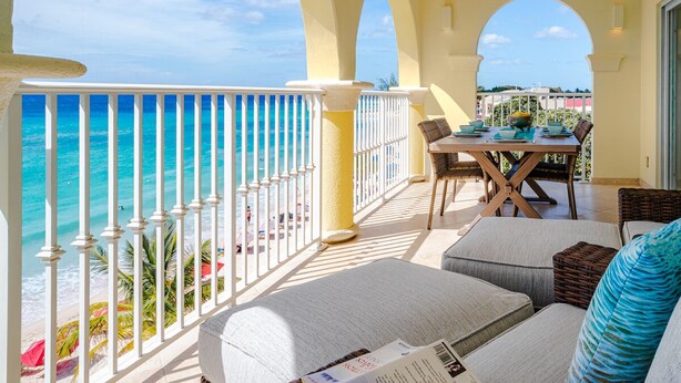 Ein Balkon mit Blick auf das Meer, ein Esstisch mit Stühlen und eine Couch mit Kissen.