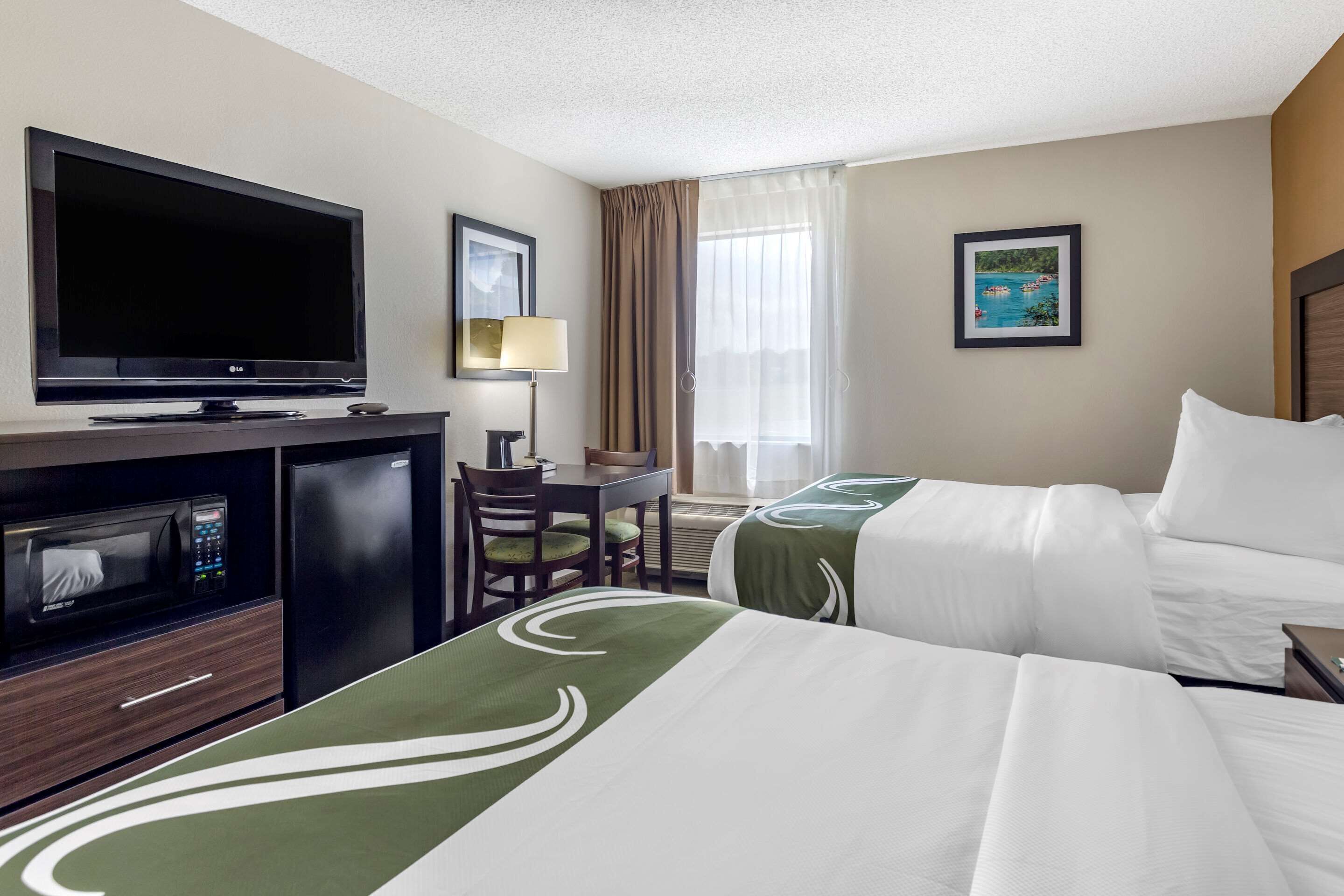 A hotel room with two beds, a TV, a desk with a chair, a microwave, and a refrigerator.