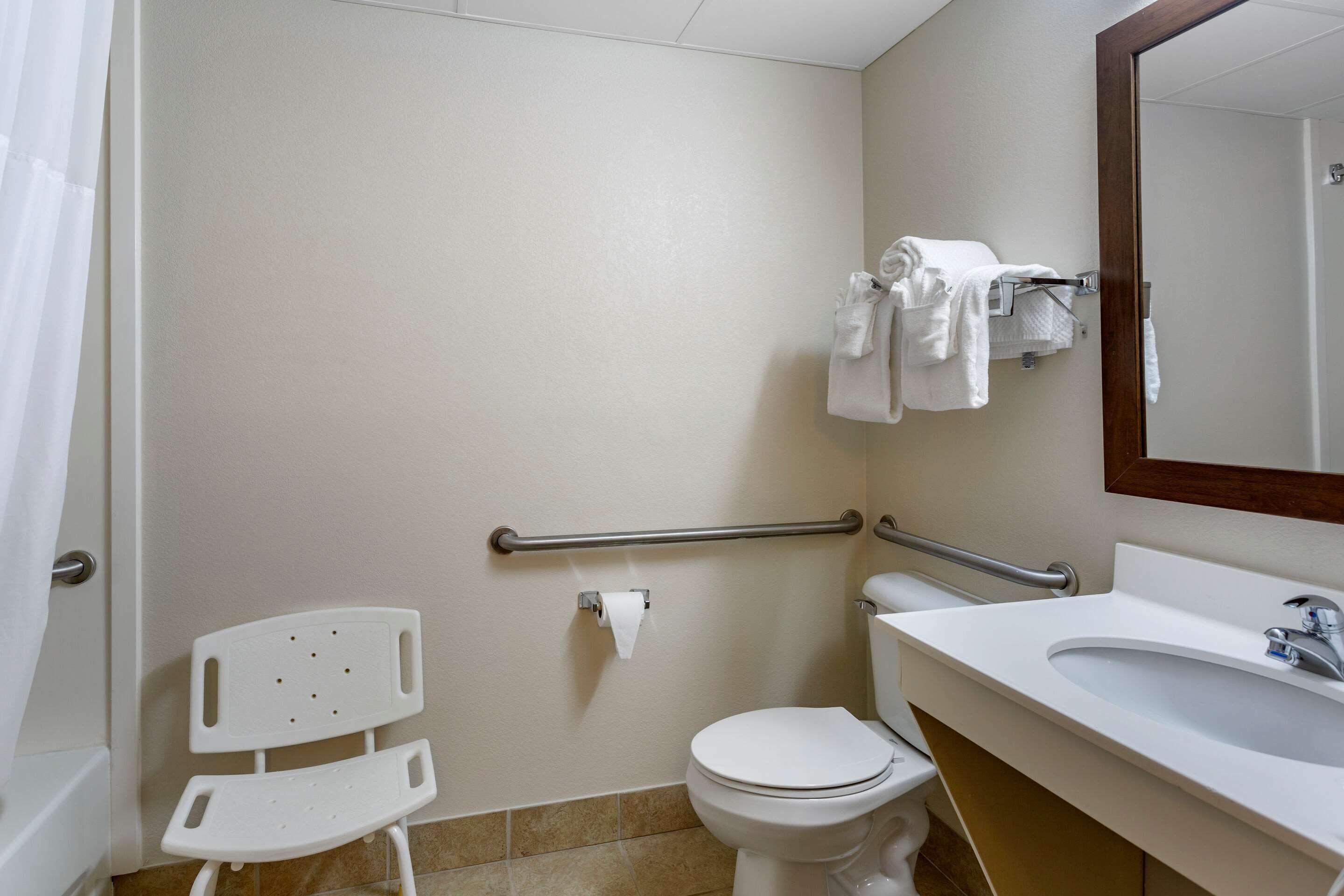 Une salle de bain avec des toilettes blanches, un lavabo, un miroir et une barre d’appui.
