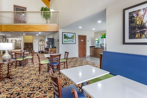 A hotel lobby with a high ceiling, a balcony with plants, a dining area with tables and chairs, and a framed picture on the wall. - Quality Inn Ocoee - Cleveland East (Ocoee)