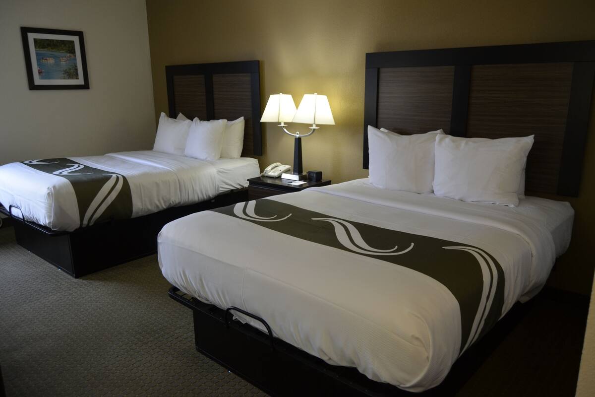 A hotel room with two beds, a nightstand with a lamp, and a framed picture on the wall.