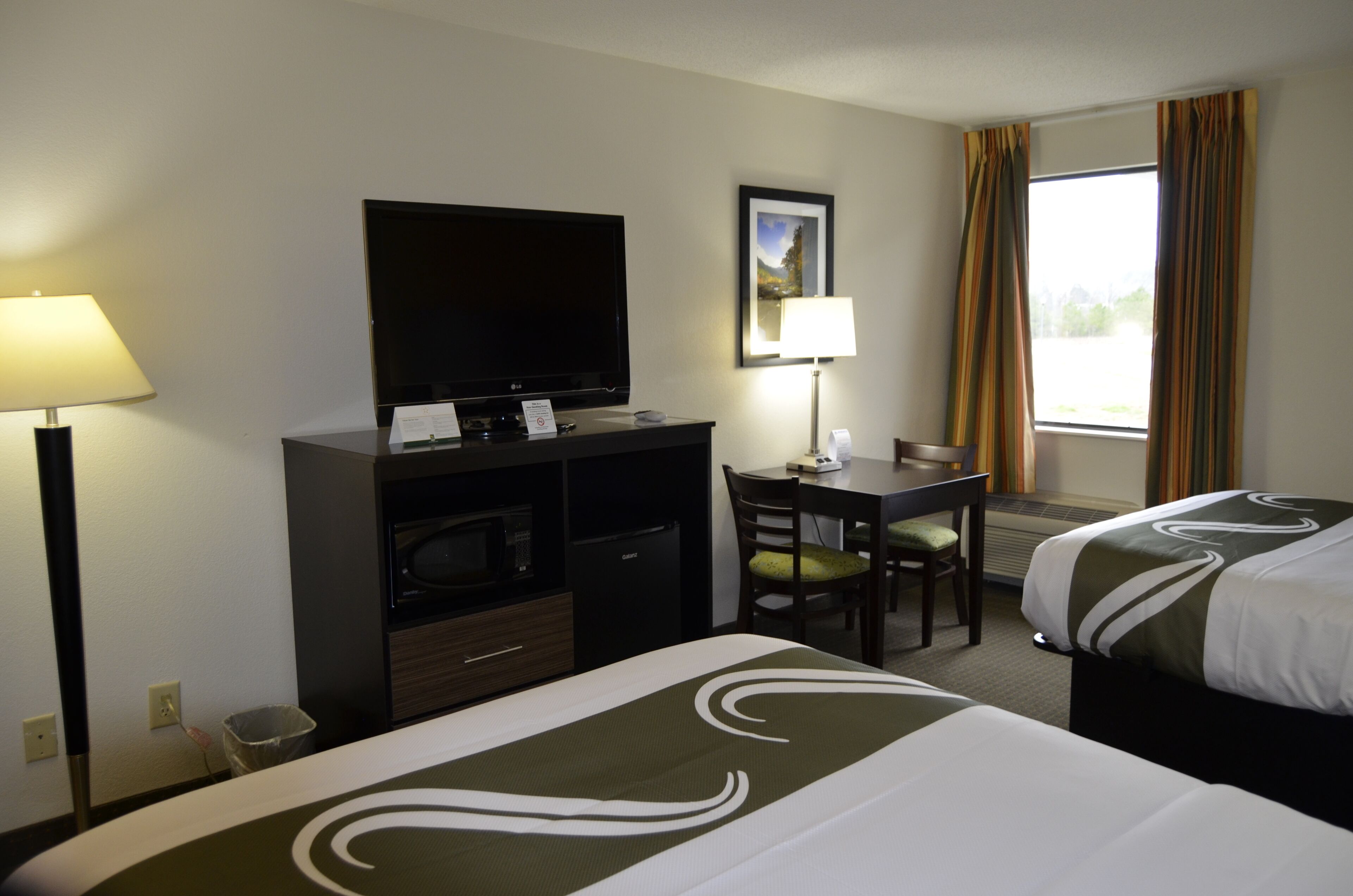 A hotel room with a bed, a desk, a television, a chair, and a window with curtains.