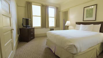 A hotel room with a large bed, a television on a dresser, a window with curtains, a lamp, and a framed picture on the wall.