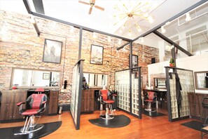 A modern barbershop with brick walls, multiple barber chairs, and a ceiling fan.