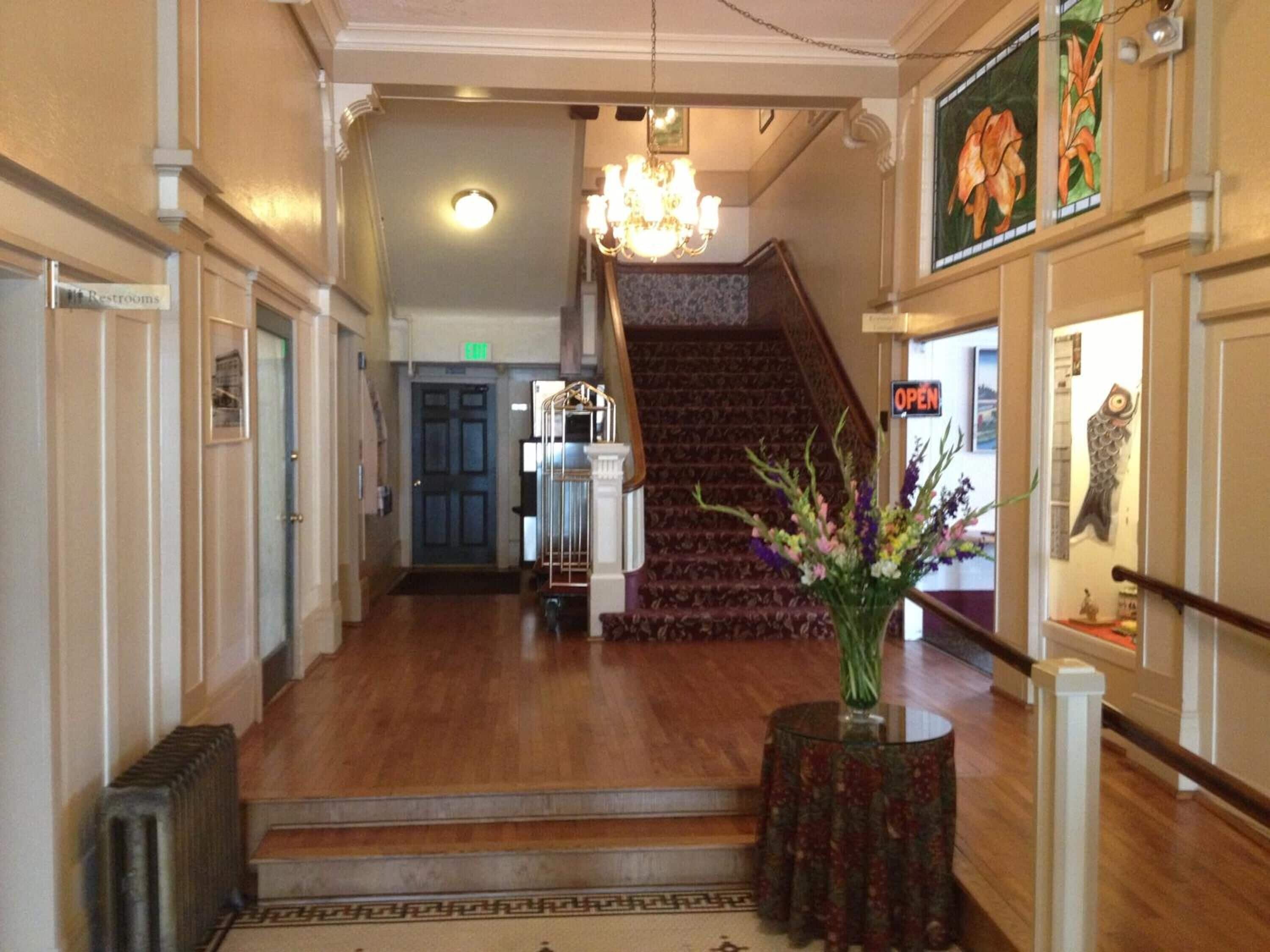 A hotel lobby with a wooden floor, a staircase, a chandelier, and a sign indicating the restroom.