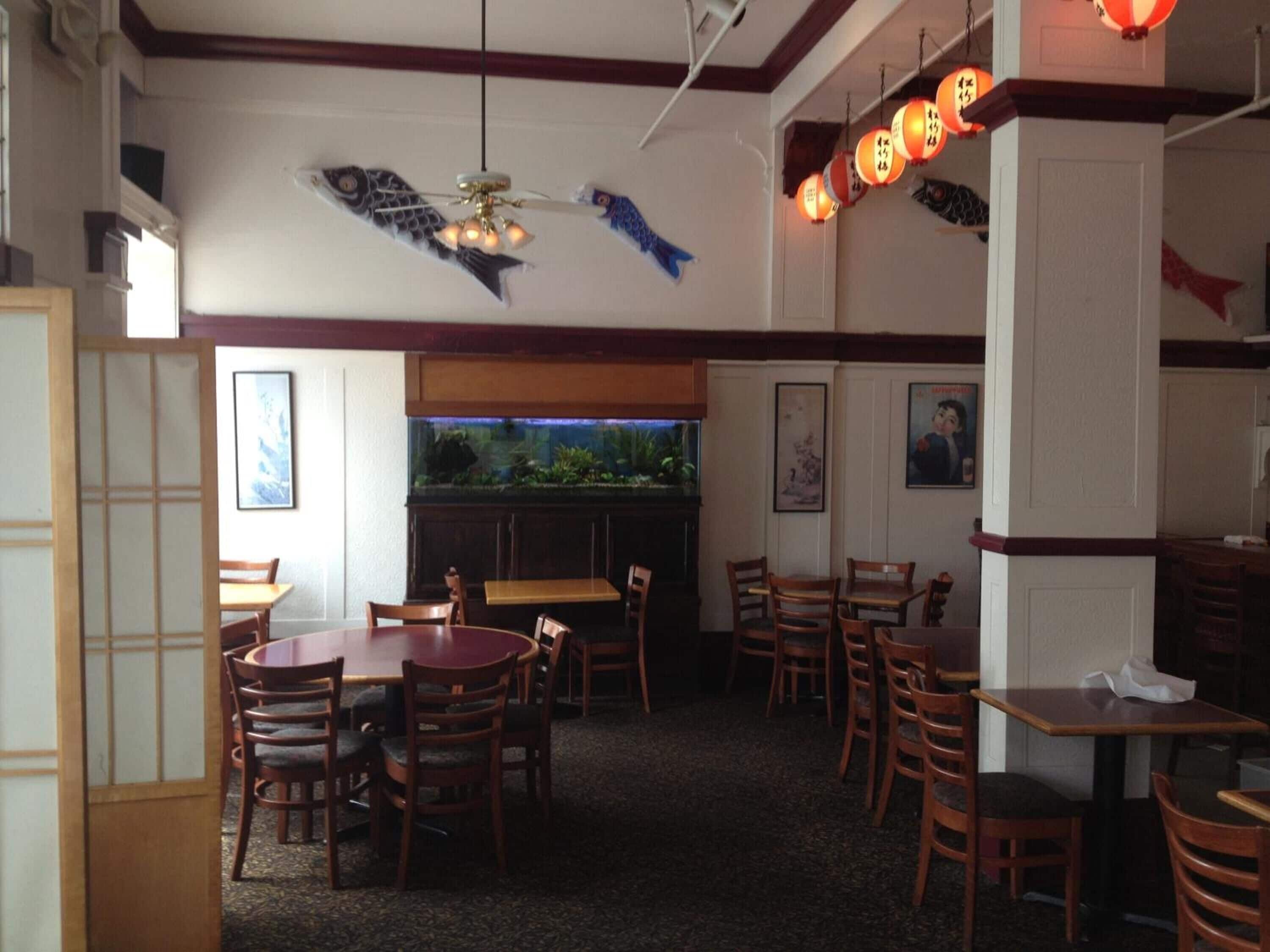 Interior de restaurant amb moble de fusta, sostre amb motius de peix i decoració tradicional japonesa.