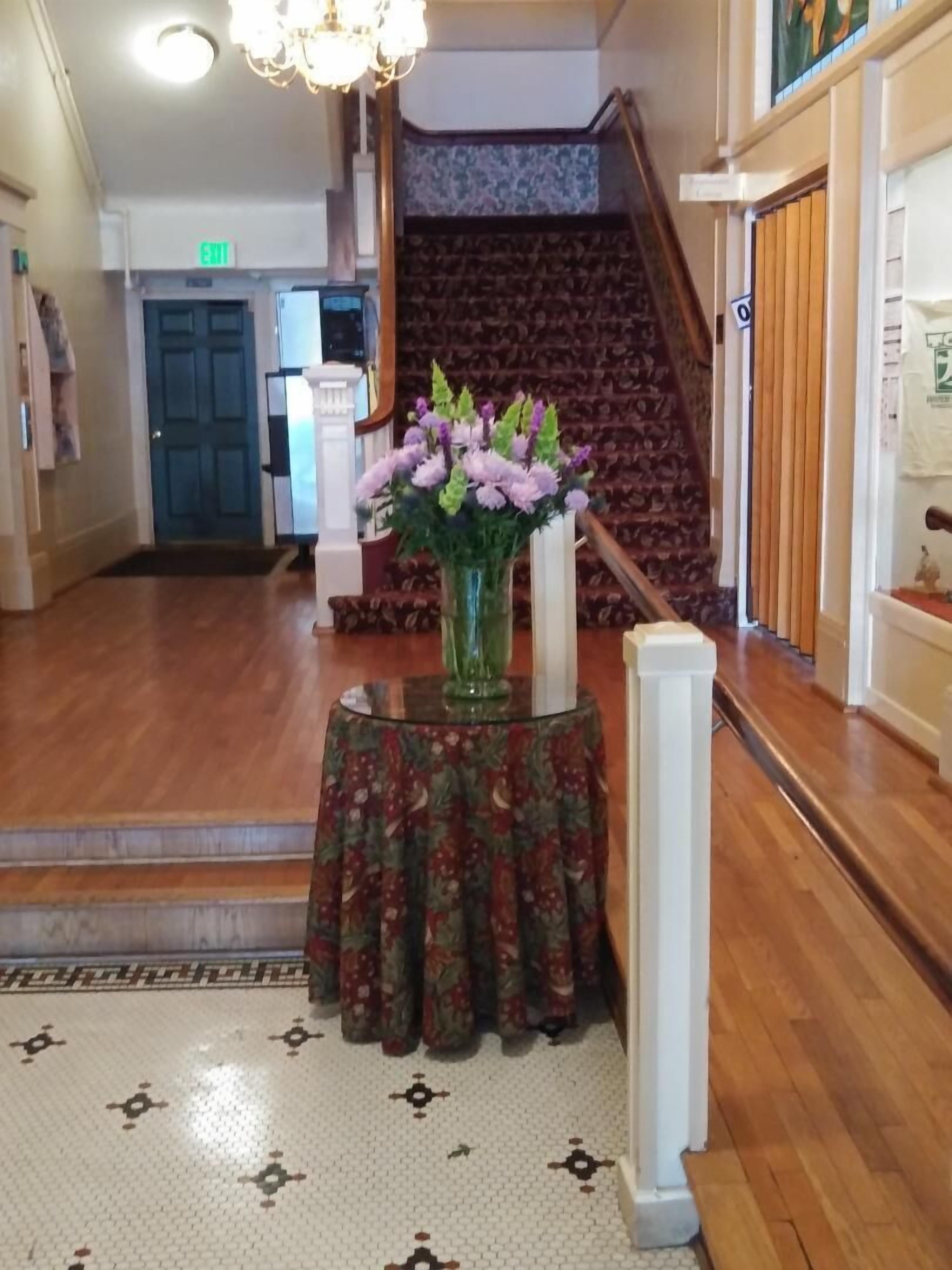 Un vestíbulo con piso de madera, un tapete estampado, un jarrón floral sobre una mesa y una escalera al fondo.