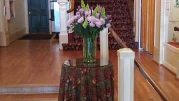 Un hall d’entrée avec un escalier, un vase rempli de fleurs et un tapis à motifs.