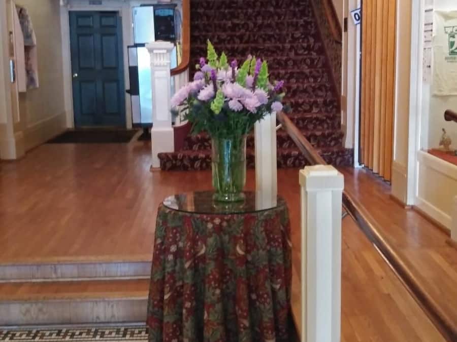 Un vestíbulo con una escalera, un jarrón con flores y una alfombra estampada.