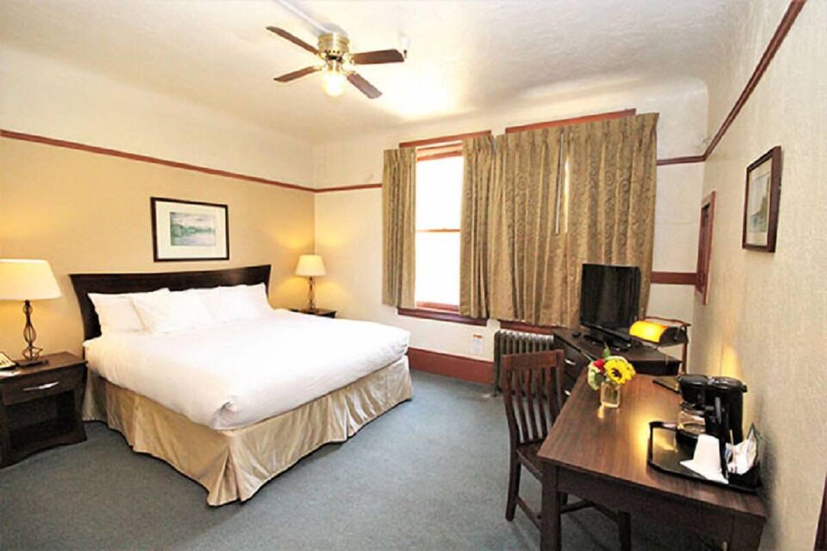 A hotel room with a bed, bedside table, lamp, chair, table, and a ceiling fan.