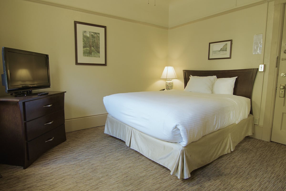 A hotel room with a bed, a television on a dresser, and two framed pictures on the walls.