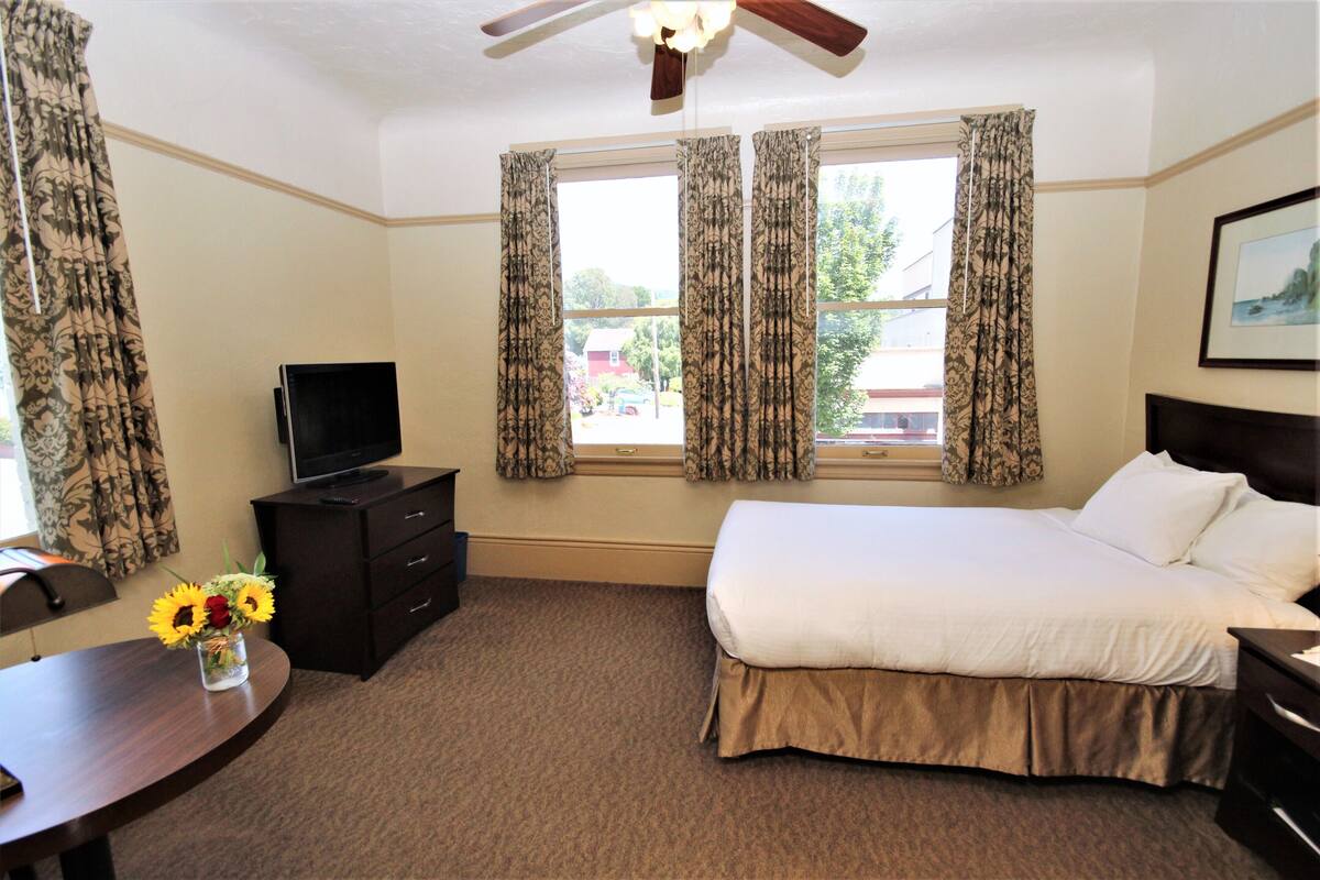 A hotel room with a bed, a desk, a TV, and a window with curtains.