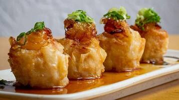 Un plat de raviolis frits, dorés à l’extérieur et nappés d’une sauce brillante, le tout garni d’oignons verts.