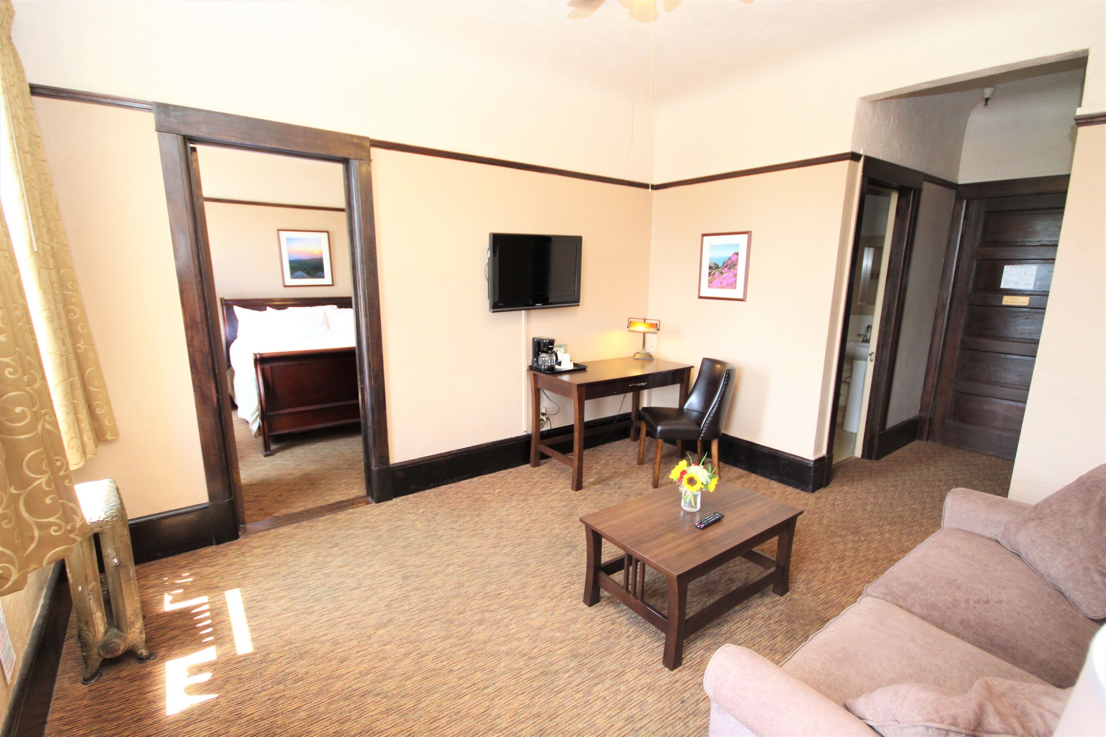 A hotel room with a sofa, a coffee table, a TV, and a desk.