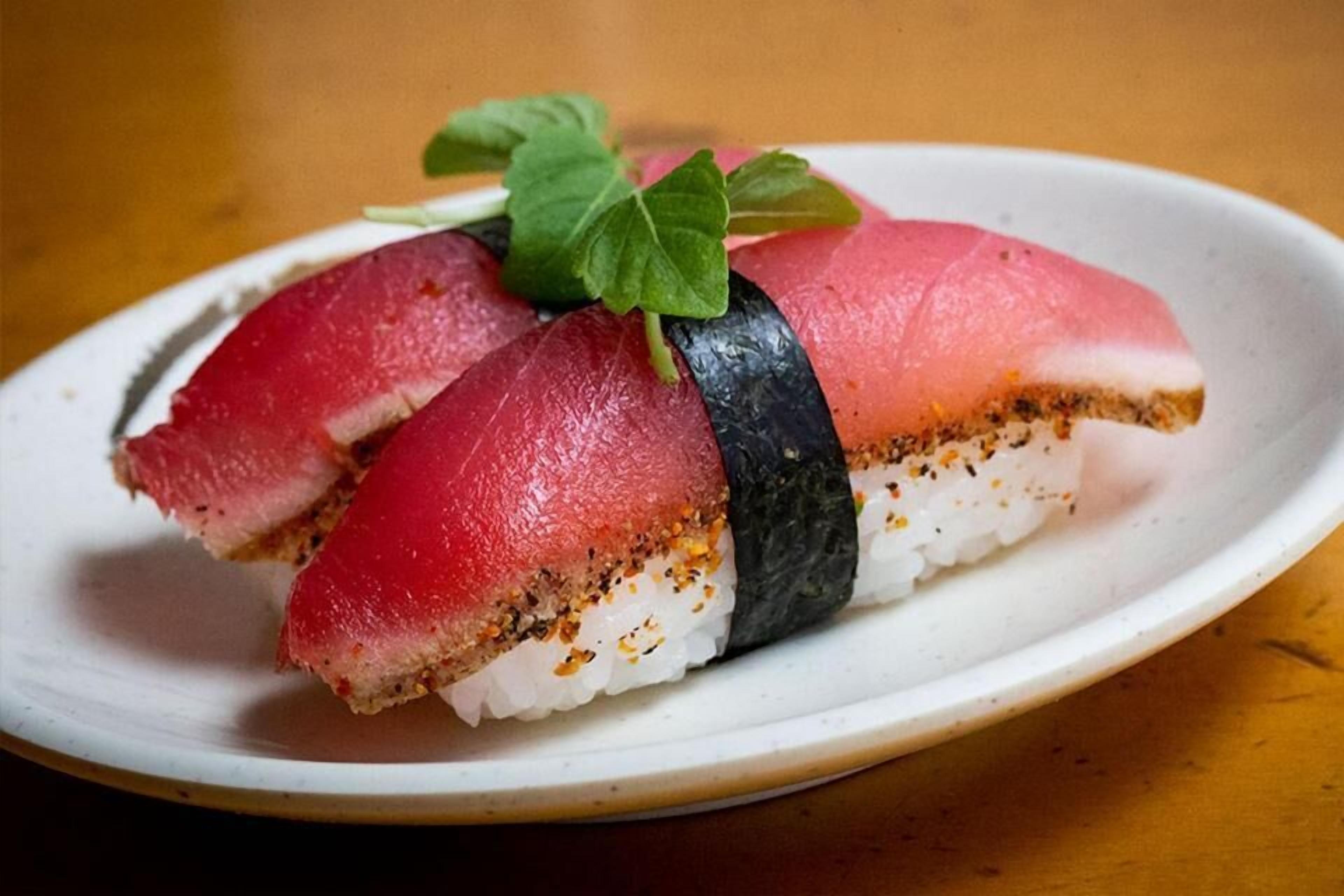 Un plato con un rollo de sushi, que incluye una loncha de pescado y una guarnición de hoja.