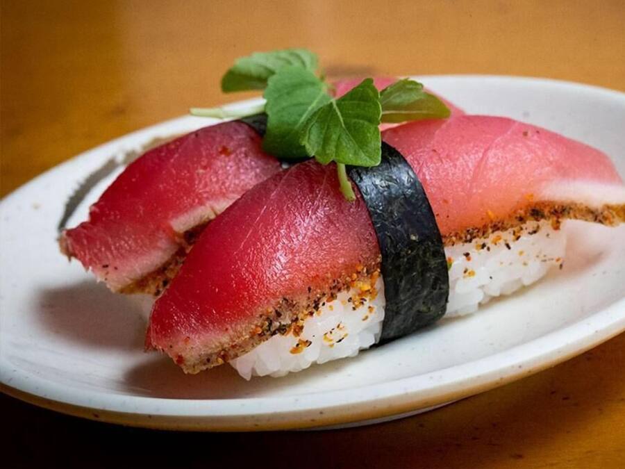 A plate with a sushi roll, including a slice of fish and a leaf garnish.