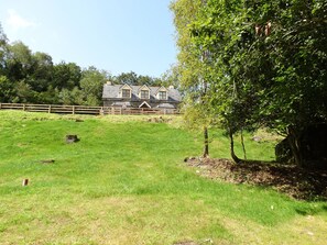 A house with a stone facade, multiple windows, and a wooden fence in a grassy field. - The River House, Nature Reserve Glengarriff (Glengarriff)