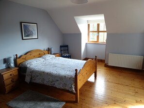 Une chambre avec un lit en bois, une table de chevet, une chaise, un radiateur et une fenêtre donnant sur un paysage verdoyant.