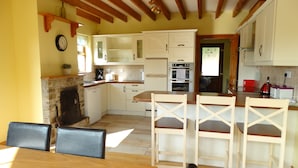 A kitchen with white cabinets, a wooden dining table, and a stone fireplace. - The River House, Nature Reserve Glengarriff (Glengarriff)