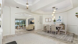 Un'ampia sala da pranzo con soffitto alto e illuminazione a sospensione, una grande finestra con vista sull'esterno e un tavolo imbandito con sedie.