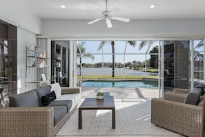 Uma sala de estar moderna com vista para a piscina, móveis de vime e um ventilador de teto.