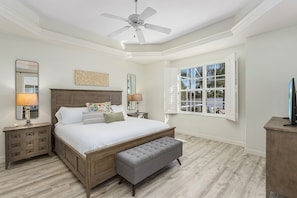 Quarto com cama grande, ventilador de teto, janela com persianas e mesa de cabeceira com abajur.