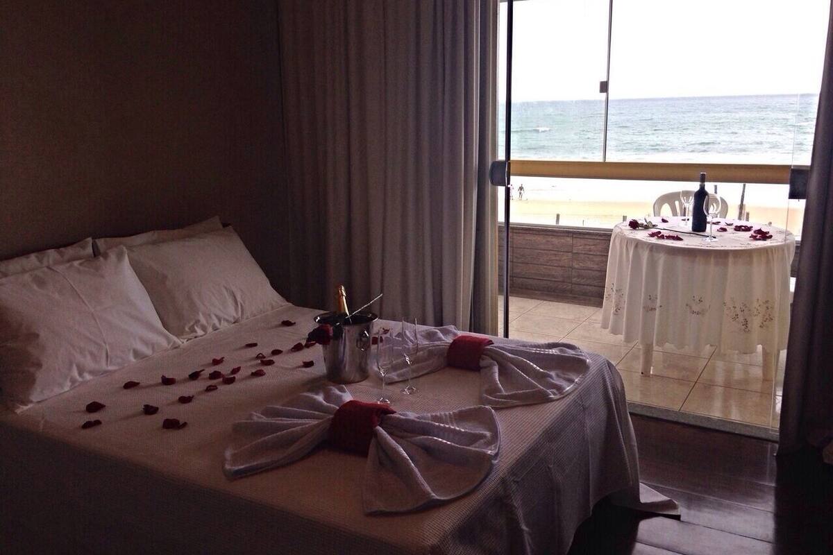 Quarto de hotel com cama, varanda com mesa e vista para o mar.