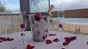 Mesa para dos con botella de champán, copas y pétalos de rosa.