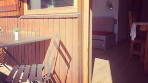 A wooden deck with a table and chairs, a bench, and a view of mountains through a window. - Fully renovated studio cabin for 2-4 people in Tignes le lac   (Le Lac de Tignes)