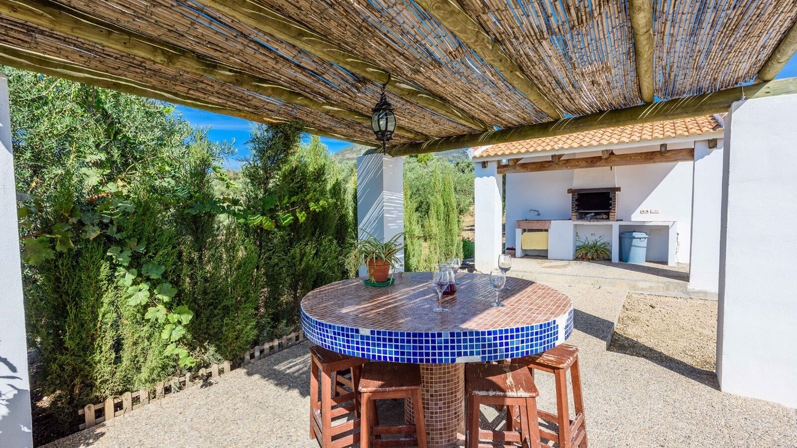 Ein runder Tisch mit blau gefliestem Rand, umgeben von Holzstühlen, unter einer Bambuspergola.