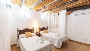 Ein Zimmer mit zwei Betten, Holzbalken an der Decke und einem Fenster mit Vorhängen.