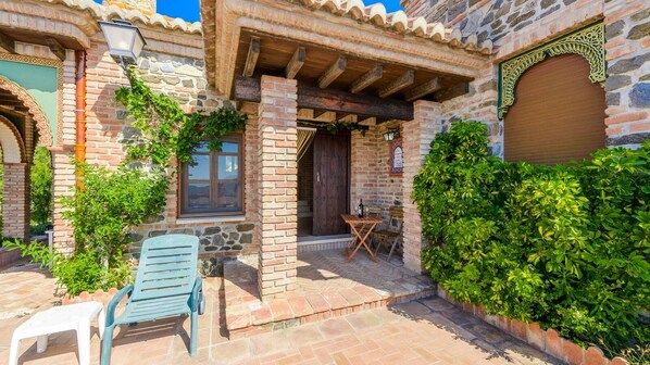 A stone building with a wooden pergola, a wooden door, and a small outdoor seating area with a table and chairs. - Alcazaba de Beas Vélez-Málaga by Ruralidays (Málaga)