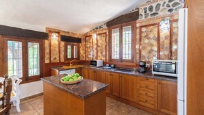 Eine Küche mit Granitarbeitsplatten, Holzschränken, einer zentralen Kochinsel mit Obstschale und einer Steinrückwand.