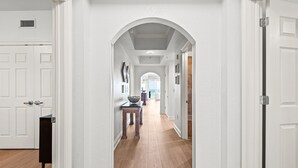 A hallway with white walls, wooden flooring, and a central archway leading to another room. - Condos directly on the Gulf (Destin)