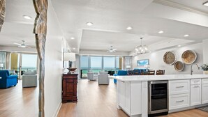 A spacious kitchen with a central island, a dining area with blue chairs, and a view of the ocean through large windows. - Condos directly on the Gulf (Destin)