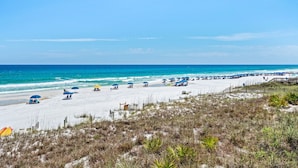 A beach with umbrellas and beach chairs, a wooden walkway, and a clear blue sky. - Condos directly on the Gulf (Destin)