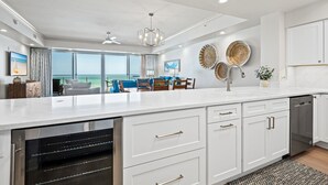 A modern kitchen with a large island, white cabinetry, and a view to the outdoors. - Condos directly on the Gulf (Destin)