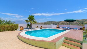 A swimming pool with a view of the hills, surrounded by lounge chairs and a palm tree. - Ramírez Almáchar by Ruralidays (Málaga)