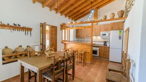 A rustic kitchen with wooden cabinets, a dining table, and a built-in oven. - Ramírez Almáchar by Ruralidays (Málaga)