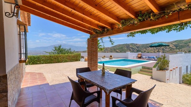 A patio with a table and chairs, a swimming pool, and a view of the hills. - Ramírez Almáchar by Ruralidays (Málaga)