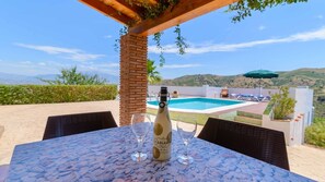 A table with a bottle of wine and two glasses, a pool, and a view of hills in the background.