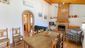 A dining area with a wooden table and chairs, a fireplace, and a cozy seating area with patterned cushions. - Ramírez Almáchar by Ruralidays (Málaga)