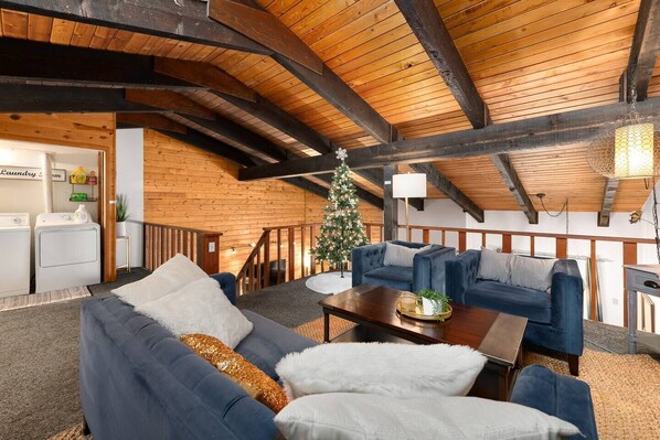 A cozy living room with a high wooden ceiling, a Christmas tree, and a sofa set.