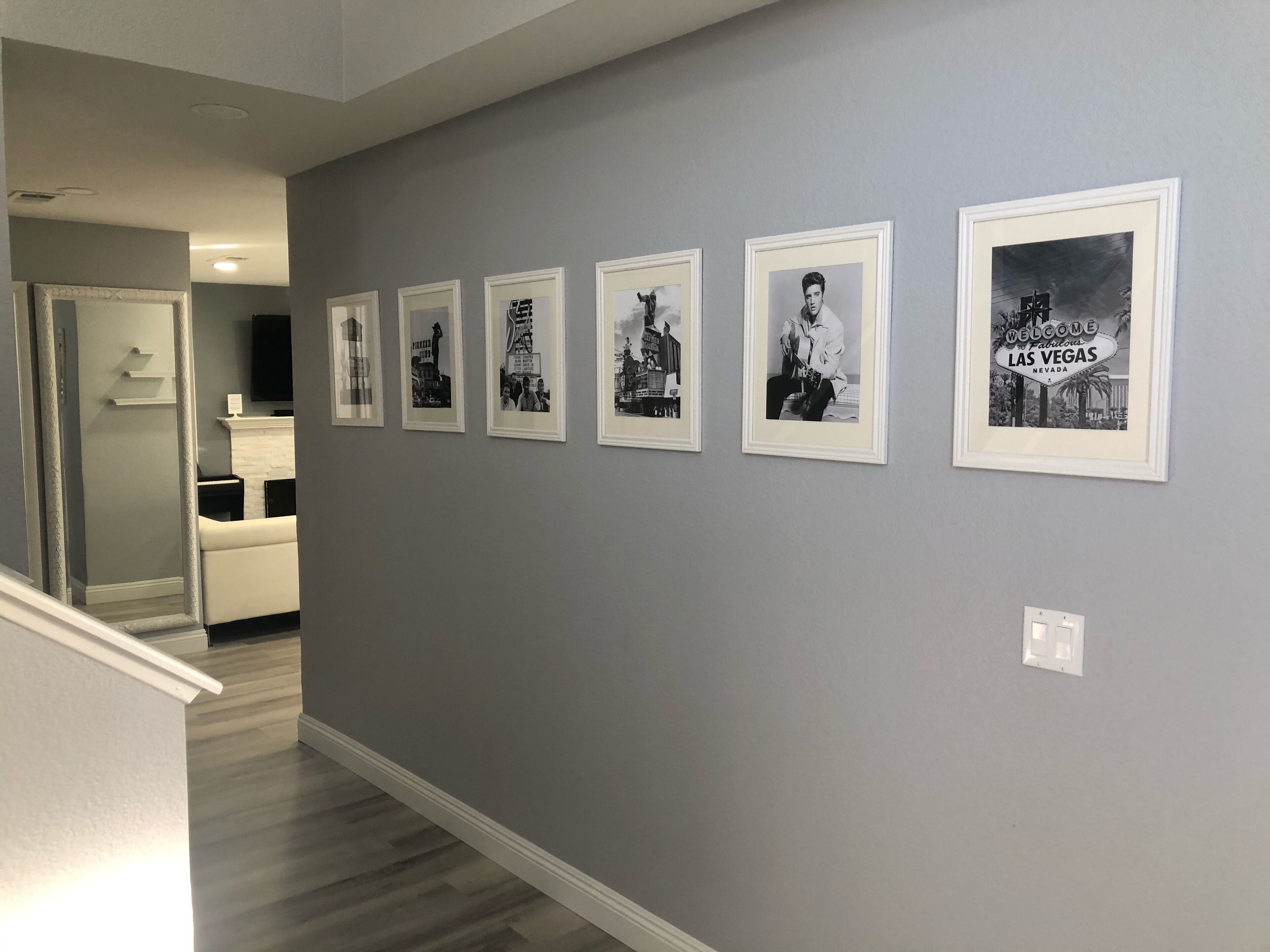 A hallway with a series of framed pictures on the wall, a white door, and a staircase leading to another room.