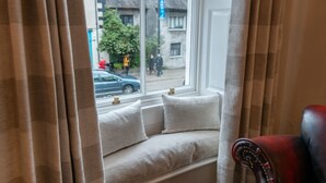 A window seat with cushions, a red chair, and a view of a street with buildings and a blue sign. - Forrest's Townhouse -  Two adjoining apartments with shared private hallway (Kendal)