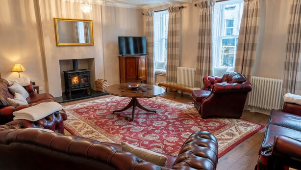 A cozy living room with leather sofas, a fireplace, a television, and a large window with curtains. - Forrest's Townhouse -  Two adjoining apartments with shared private hallway (Kendal)