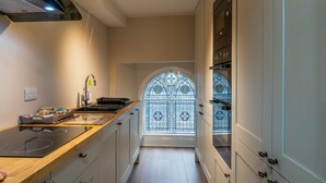 A narrow kitchen with a built-in stove, a sink, and cabinets. A stained glass window is visible in the background. - Forrest's Townhouse -  Two adjoining apartments with shared private hallway (Kendal)