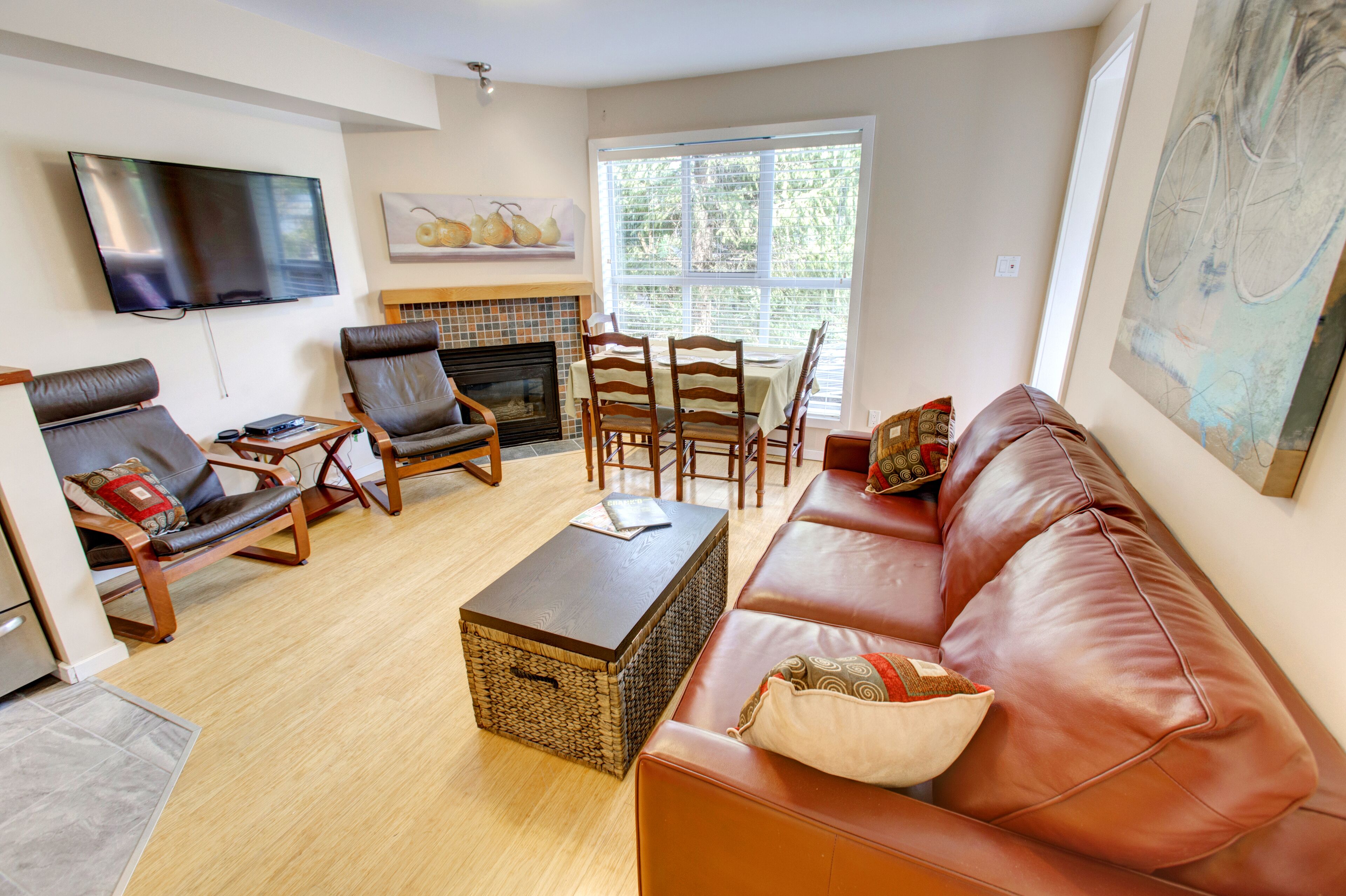 Un salon comprenant un canapé en cuir, deux fauteuils, une table basse, une cheminée, une table à manger avec des chaises et un téléviseur fixé au mur.